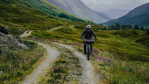 Gravel-Biker fährt auf einem Weg durch ein grünes Bergtal.